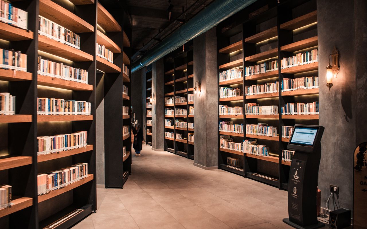 about-02 A spacious library featuring tall wooden bookshelves filled with books and ambient lighting.